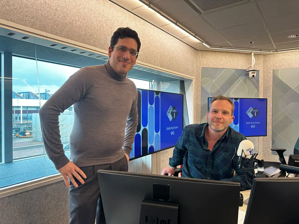 Twee collega's presenteren op een congres, voor een blauwe wand met schermen
