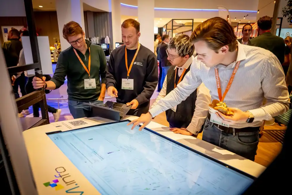 Vier mensen gebogen over een verlichte maquettetafel tijdens een bijeenkomst