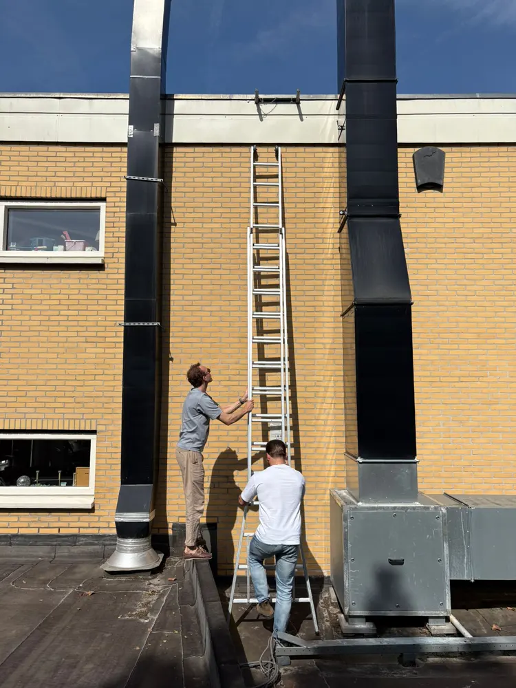 Twee collega's van CCS op het dak van een woongebouw, bij de installaties en een ladder naar het bovendak
