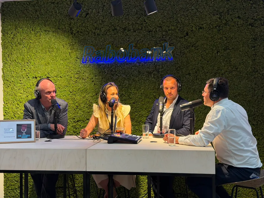 Vier mensen aan tafel op een podium, met een groene wand erachter