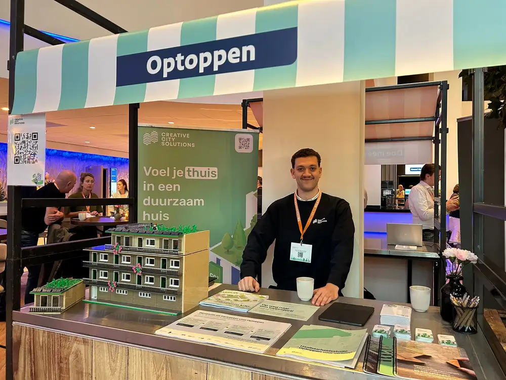 De stand van CCS op een beurs, met maquette, onder het bord Optoppen