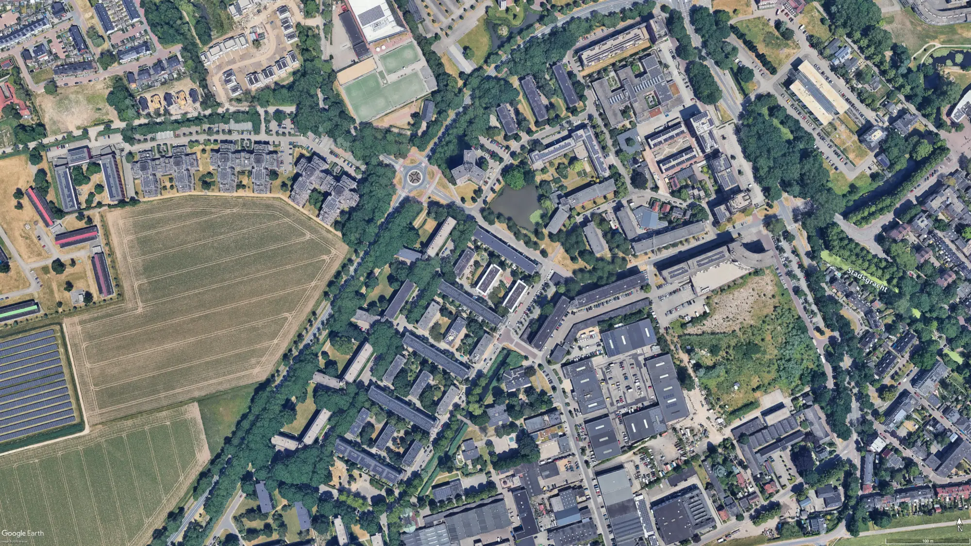Luchtfoto van een woonwijk in Wageningen: flats tussen bomen, akkers aan de westkant en bedrijfshallen aan de zuidkant